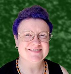 a woman with purple hair and glasses smiling at the camera, against a green background