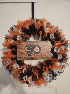 an orange and black mesh wreath with the philadelphia flyers logo is hanging on a door