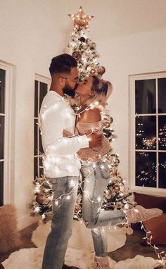 a man and woman kissing in front of a christmas tree