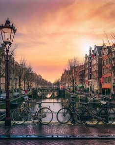 bicycles are parked along the side of a canal at sunset or dawn in an old european city