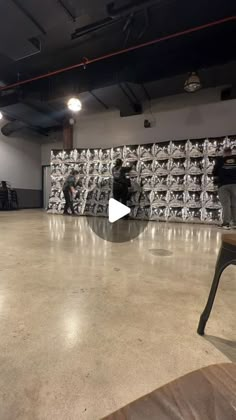 two men are standing in front of a wall with stacks of boxes on it and one man is holding a skateboard