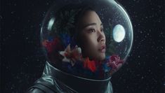 a woman in an astronaut's suit with flowers on her head and the moon behind her