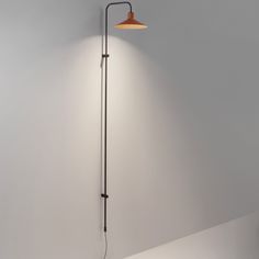 a lamp that is on the side of a white wall with a black pole attached to it