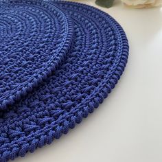 a crocheted blue rug next to a white rose on a table with flowers in the background