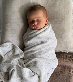 a baby wrapped in a blanket sleeping on a pillow