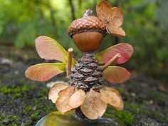 a small figurine made out of leaves and acorns sitting on top of a rock