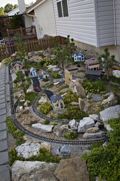 a model train set is in the middle of a yard with rocks and trees around it