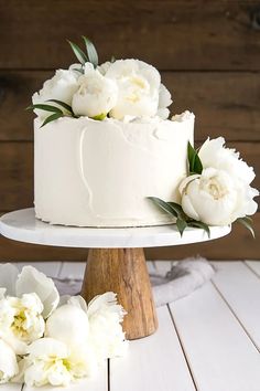 there is a white cake with flowers on the top and bottom, sitting on a wooden stand