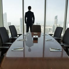 a man standing at the end of a conference table in front of a large window