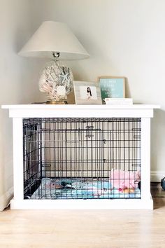 a dog cage sitting on top of a white table next to a lamp and pictures