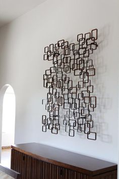 a wall sculpture made out of metal squares on a white wall next to a wooden cabinet