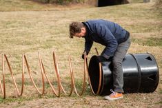 a man is leaning on a barrel and bending over to pick up something from the ground