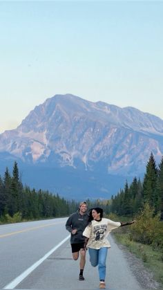 two people running down the road with mountains in the background