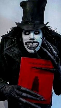 a man dressed in black holding a red book with his hands and face painted white