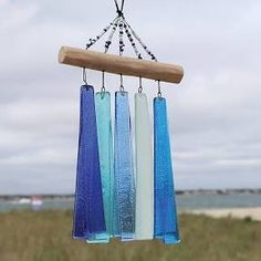 three blue, white and clear glass wind chimes hanging from a wooden pole in front of the ocean