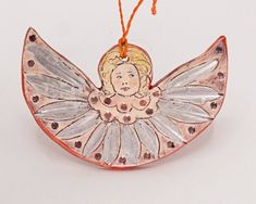 a ceramic angel ornament hanging from a string on a white surface with an orange cord