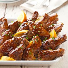 chicken wings with orange slices and garnishes on a white plate next to silverware