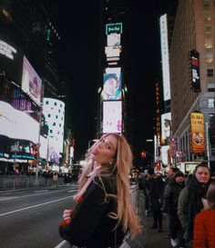 a woman standing in the middle of a busy city street at night with billboards on buildings