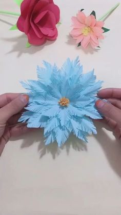 two hands are holding paper flowers on a table