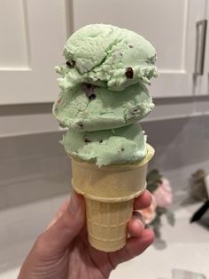 a hand holding an ice cream cone filled with mint green chocolate chip icecream