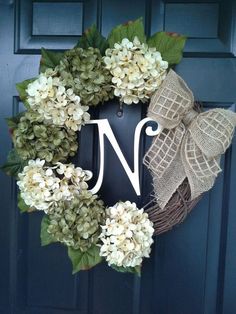 a wreath with the letter n is hanging on a blue door and it has white flowers