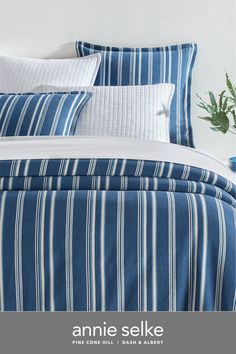 a bed with blue and white striped comforter next to a potted plant on a table