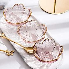 three pink glass dishes sitting on top of a white plate with gold trimmings