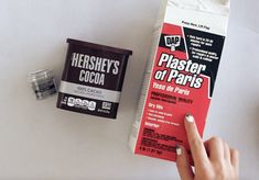 a person pointing at a carton of chocolate next to a container of cocoa and a can of hershey's cocoa