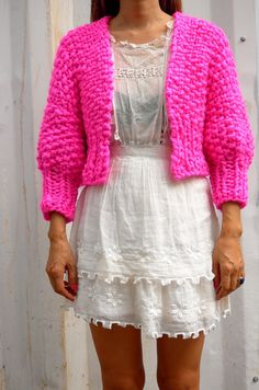 a woman wearing a white dress and pink cardigan standing in front of a wall