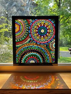 a colorful art piece sitting on top of a wooden table in front of a window