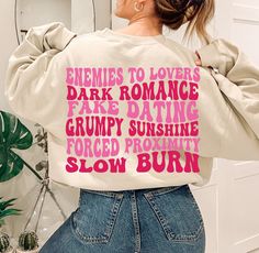 a woman wearing a white sweatshirt with pink writing on it that says, sometimes to lovers dark romance fake dating grumpy sunshine forced proximity slow burn