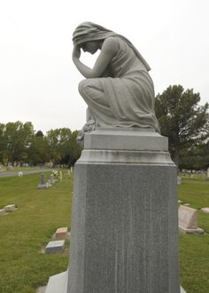 a statue sitting on top of a cement slab in a cemetery next to a grass covered field