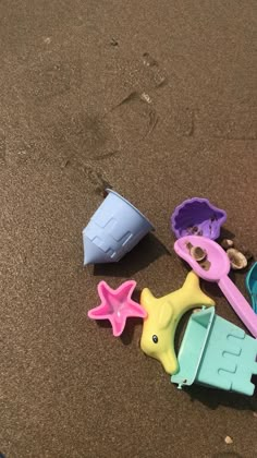 several toys are laying on the sand with one toy in it's mouth and two plastic shovels