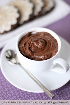 a white plate topped with a cup of chocolate pudding next to crackers on a purple table cloth