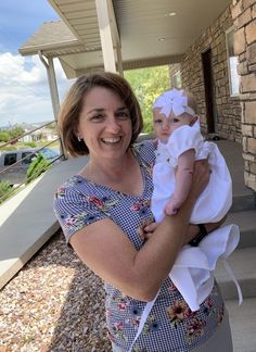 a woman holding a baby in her arms on the front steps of a house,