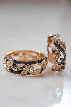 two wedding bands with leaves and scrolls on them, sitting on a white table top