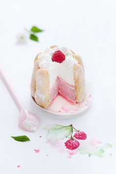 a white cake with raspberry filling on a plate next to a pink spoon