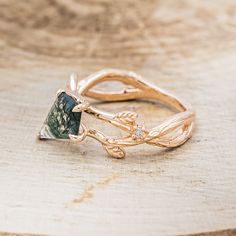 two gold rings with green and white stones on them sitting on a wooden surface in front of a piece of wood