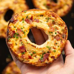 a hand holding up a cheesy bagel with bacon and green onions