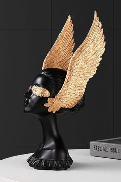 a black and gold headpiece with wings on top of a white table next to a book