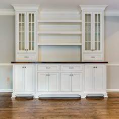 an empty kitchen with white cabinets and wood floors