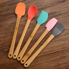 four different colored spatulas on a wooden table