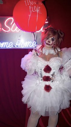 a woman dressed as a clown holding a red balloon in front of a neon sign