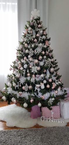 a small christmas tree with pink and white ornaments on it in front of a window