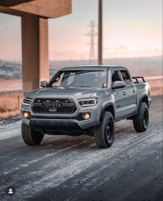 a grey toyota pickup truck driving down a road next to a tall building with snow on the ground