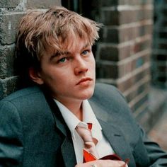 a man in a suit leaning against a brick wall with his hand on his tie