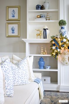 a living room decorated for christmas with blue and gold decorations on the shelves, white couches and pillows