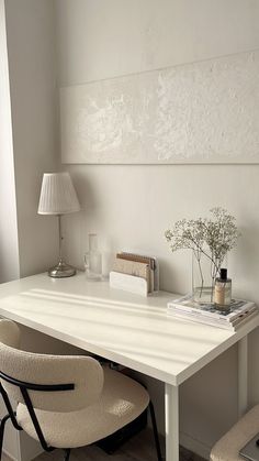 a white desk topped with a lamp next to a chair and a vase filled with flowers