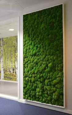 a green moss covered wall in an office setting with two windows looking out onto the woods