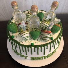 a cake decorated with green and white icing has bottles of gin in the shape of strawberries